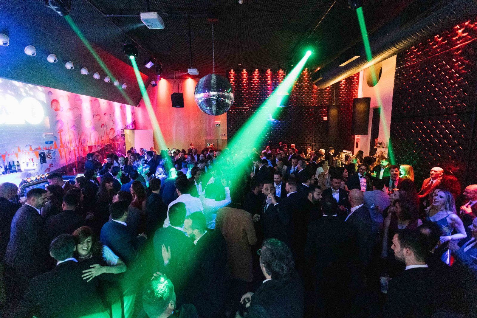 Pista de dança atravessada por feixes de luz verde, sob uma bola de espelhos