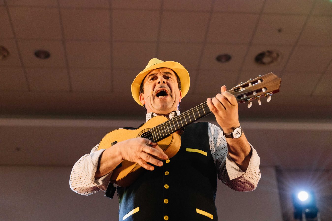 Músico de chapéu e colete a cantar e a tocar viola num evento