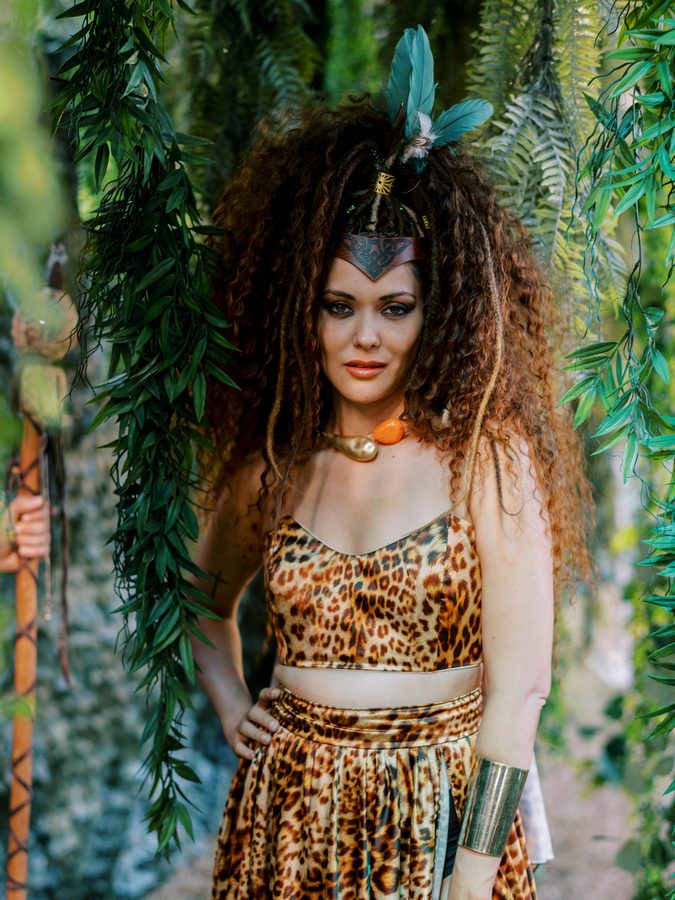 Performer com traje de leopardo e toucado de plumas, em cenário de selva no evento WILD