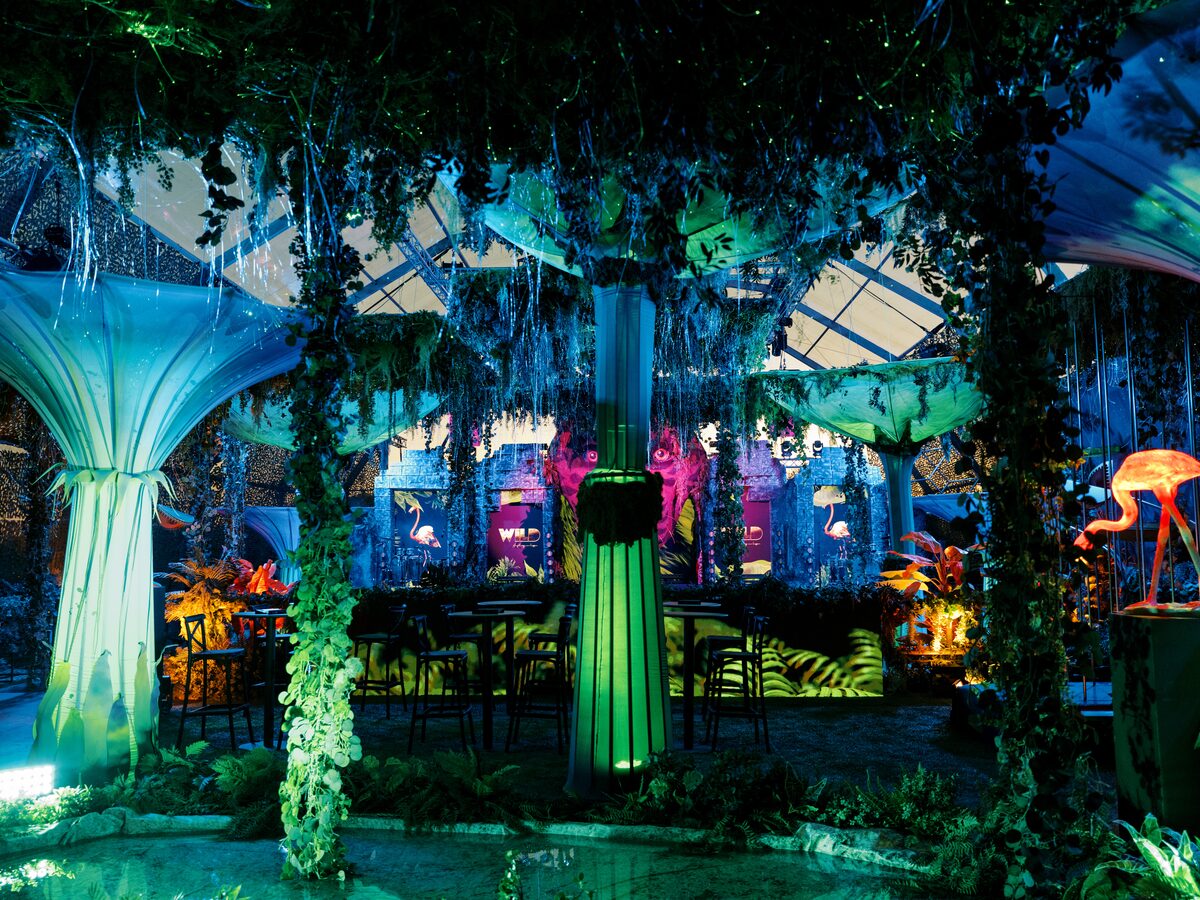 Cenário de selva com árvores luminosas e um bar iluminado a verde, no evento WILD