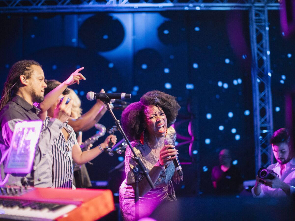 Dois cantores e um teclista em palco, sob um fundo de luzes, no evento Soul Man