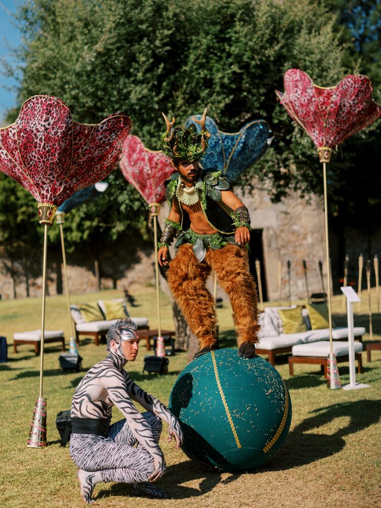 Performers em trajes de fantasia com esferas gigantes num jardim