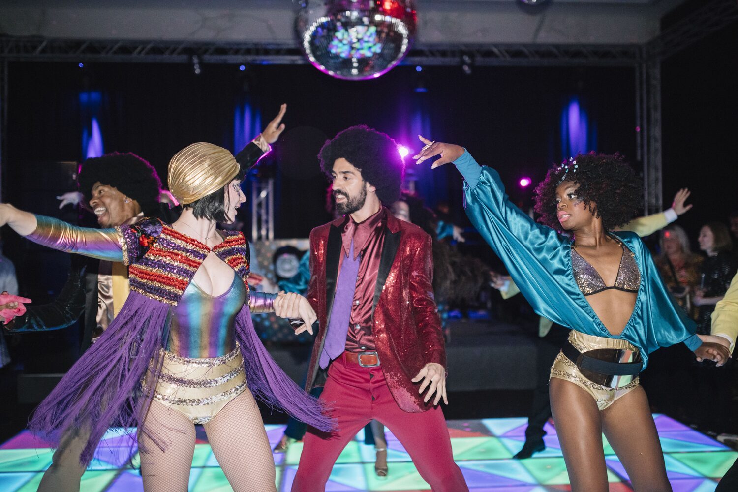 Bailarinos com fatos disco sob uma bola de espelhos